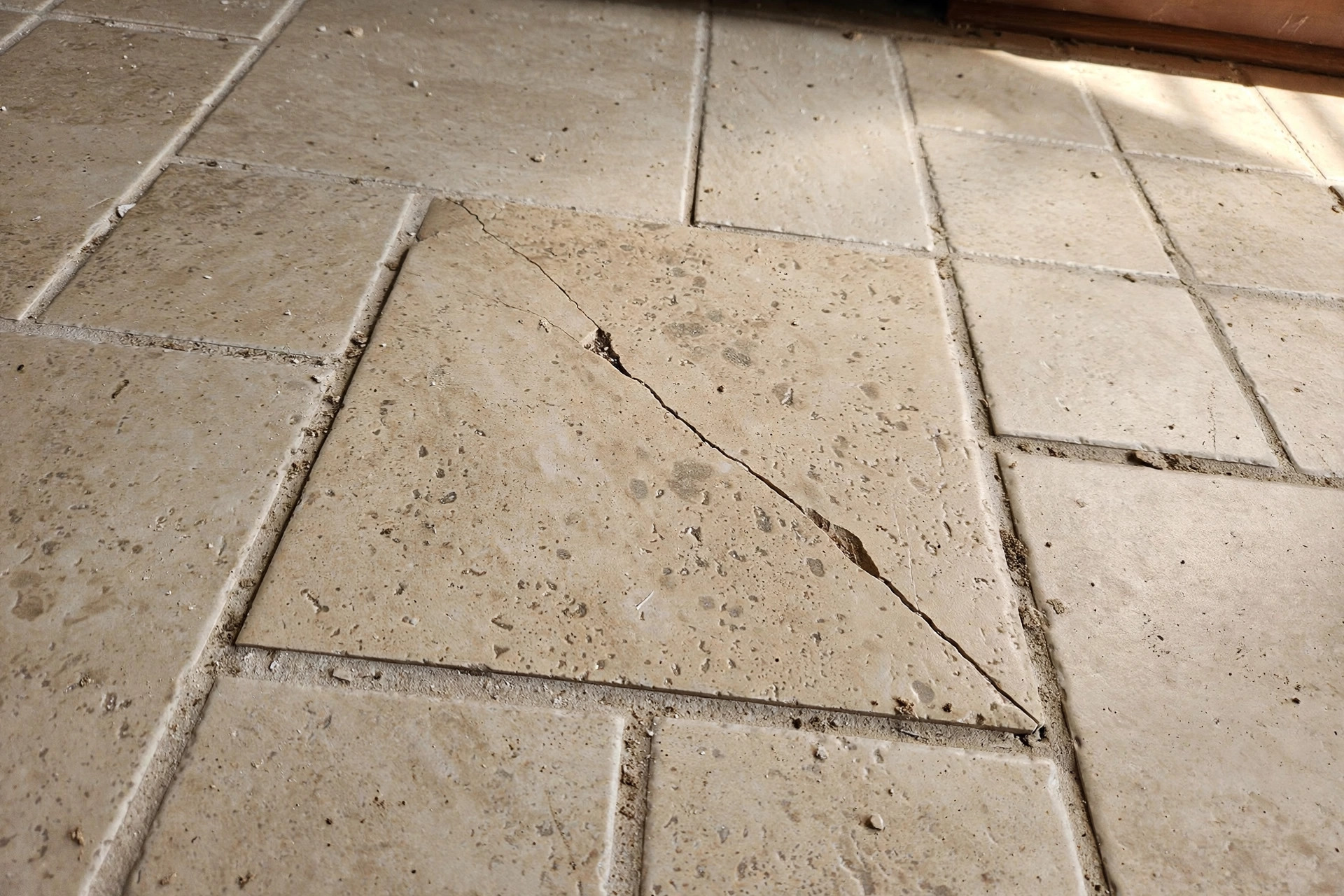 A cracked ceramic floor tile in a home kitchen before repair, part of a replacing single cracked floor tile guide