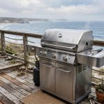 Stainless steel gas grill on a beach house deck with the best outdoor grill for coastal salt air